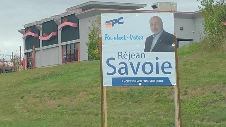 Plan moyen sur une pancarte électorale bilingue de Réjean Savoie.